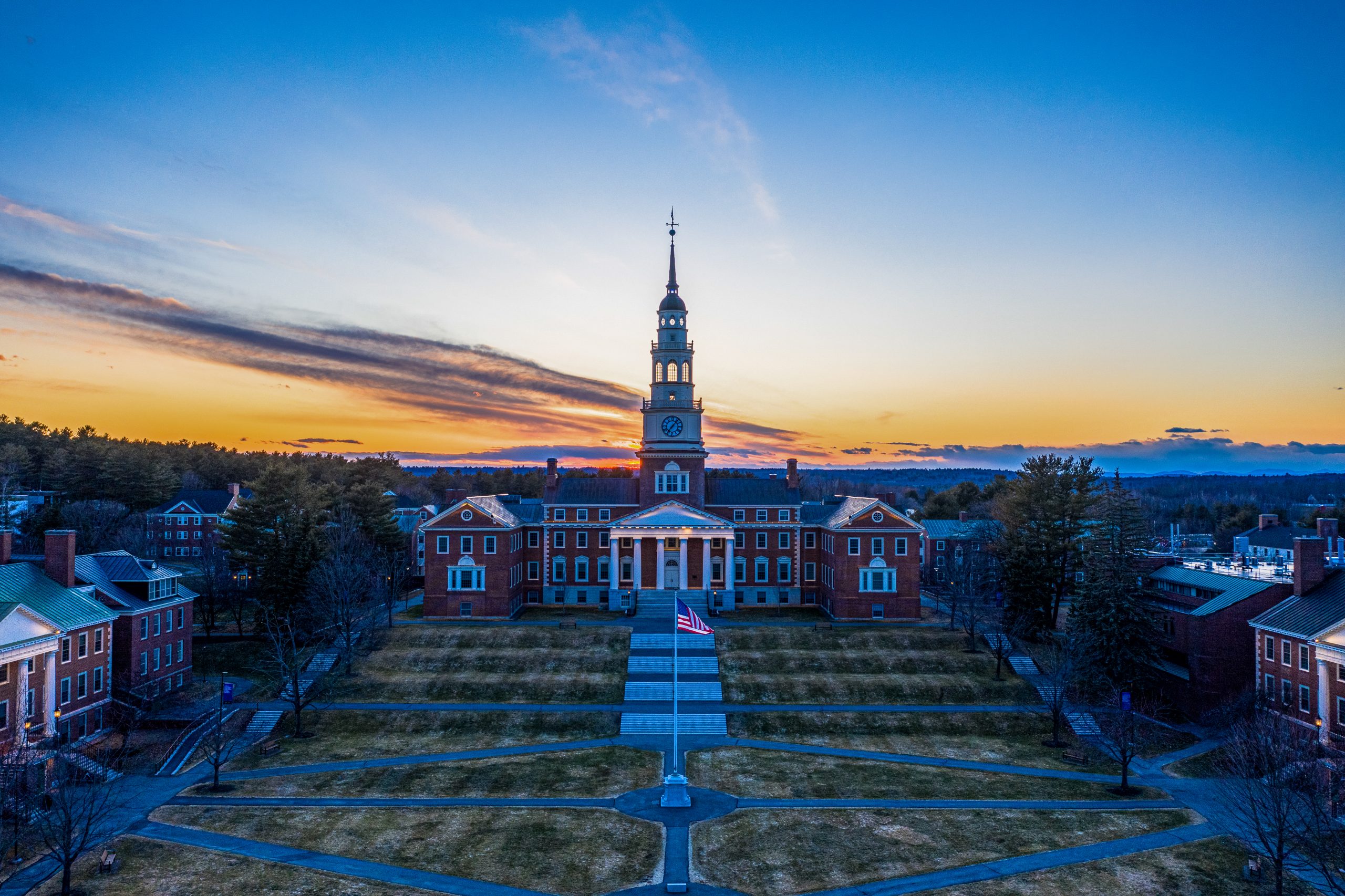 Aerial view of a university campus at sunset, featuring a prominent clock tower and landscaped grounds.