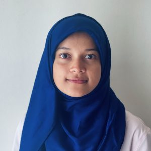 Young woman wearing a blue hijab, with a neutral expression, against a light background.