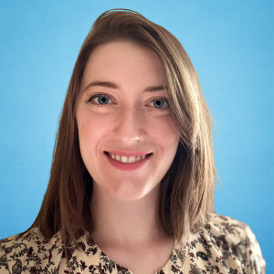 Smiling person with light brown hair and a floral shirt against a blue background.