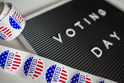 Black board with VOTING DAY text and a roll of I VOTED stickers featuring red, white, and blue designs.