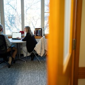 Two people in an office setting are engaged in discussion, seated by a window with natural light filtering in.